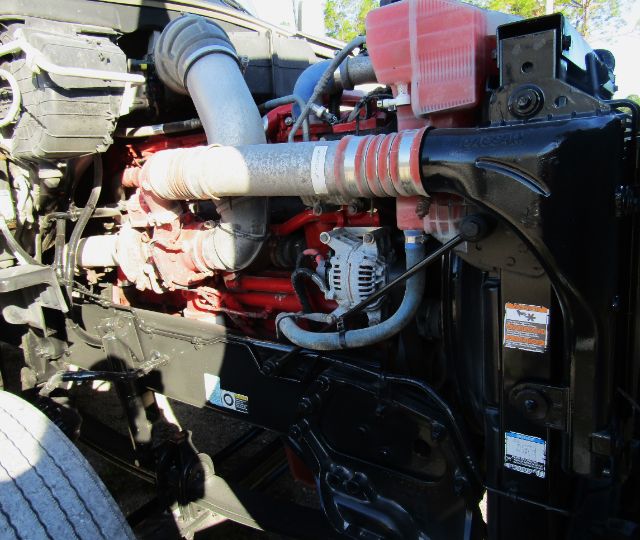 Truck engine bay showing large air intake, red-painted engine, alternator, hoses, and front chassis area.