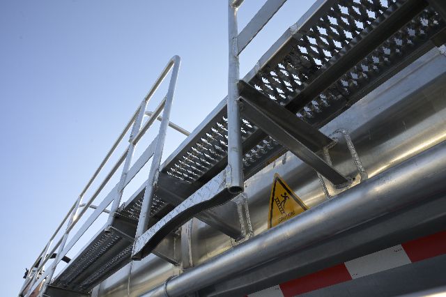 Aluminum vacuum trailer side rail and ladder detail showing a warning label and metal piping.