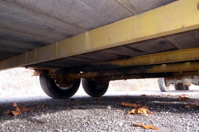 Trailer undercarriage showing tandem axles and wheels with metal frame and decking overhead.