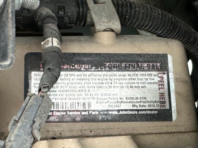 Label on engine or component with various model/engine information and a barcode, hoses and wiring around. Text includes company and dealer references, and service parts.