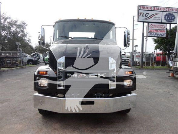 Front view of a white 2023 Mack MD6 truck in a dealership lot, with a large black grille and bumper; dealership signs in background.