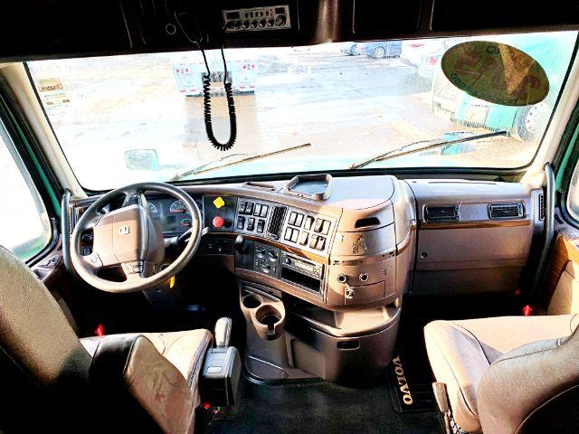 Dashboard and steering wheel of a 2015 Volvo VNL 670 truck cab interior. Visible controls on the center console, steering wheel with Volvo logo, two seats, gear shifter, dash panels, windshield.