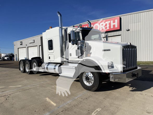 Kenworth T800 conventional sleeper truck in white, front grille, large exhaust stack, multiple rear axles, showroom lot.