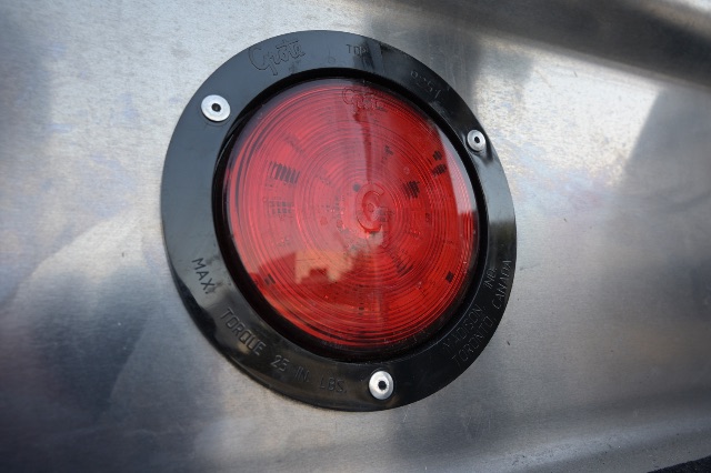 Back of aluminum trailer showing round red tail light with black bezel and mounting screws.