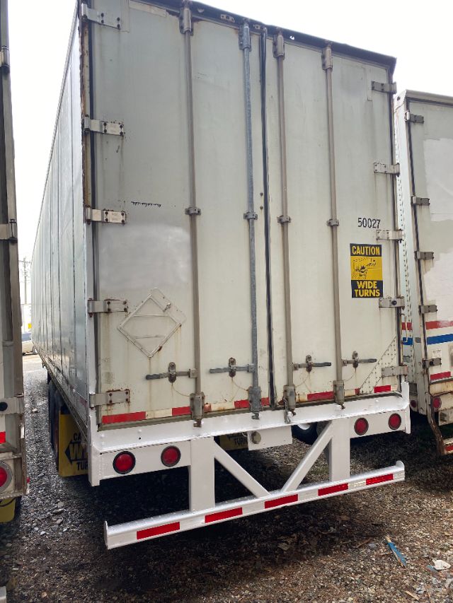Rear view of a rectangular metal trailer with double doors, caution sticker, and reflective red/white bars.