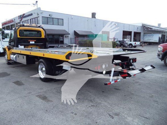 2019 International DURASTAR 4300 tow truck with flatbed in a dealership lot showing VIN plate and stock number in the background.
