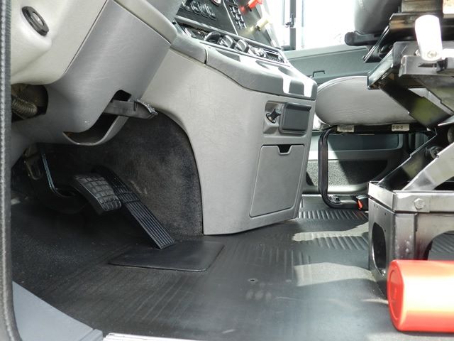 Cab/driver area of a Freightliner truck showing the accelerator and brake pedals, center console, and entry floor with rubber matting.