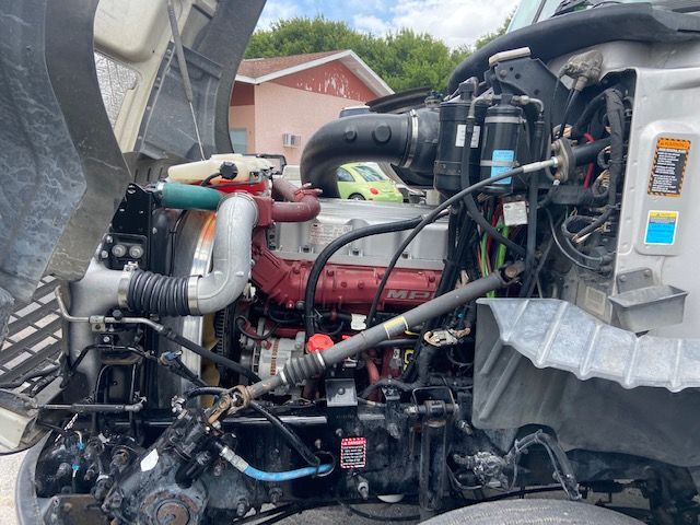 Engine bay of a 2010 Mack CXU613 conventional sleeper showing turbocharged diesel engine, hoses, wiring, radiator hoses, and air intake components.