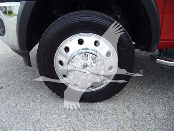 Truck wheel and chrome hubcap showing steel wheel with black tire and front fender of red Ram 5500 SLT.