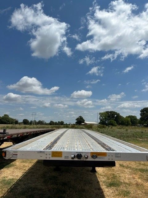 Flatbed trailer deck view from rear showing metal perforated deck and reflective markers.