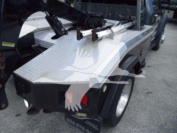 Tow truck bed area with diamond plate metal, wheel, taillights, and rear bumper. Visible text includes '855-...'? and 'truck' markings.