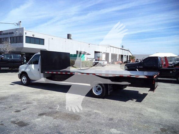 Flatbed tow truck in a used inventory lot with a long flatbed and white cab, 2011 Ford E450 may be seen.
