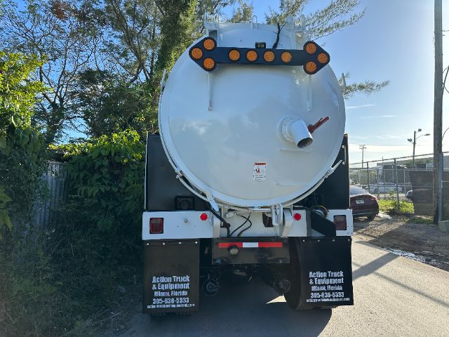 Back view of a white circular vacuum truck tank on a International heavy truck, rear lights, hoses, and mud flaps with contact text, in an outdoor lot.