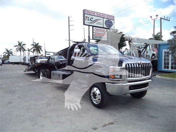 Truck on lot showing grille, cab, and flatbed behind front wheel. Visible text on sign: Truck Sales Center TLC, ETIV maybe. No clear model text on truck. VIN 1HTKTSWK6PH441635 not visible on the image itself. Plate areas not legible.