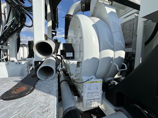 Vacuum truck equipment with large circular blower housing, hoses, and metal platform; visible labels and warning placards on white machinery.