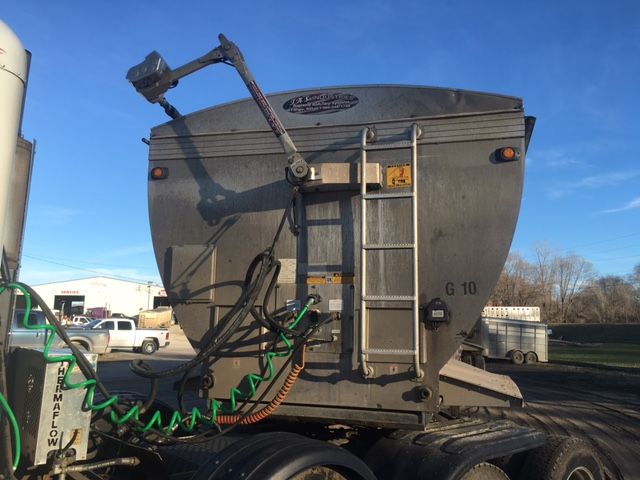 Trailer rear view with a mounted crane arm, grey hopper-style cargo box, ladder on right, coiled green hose, and various cables.