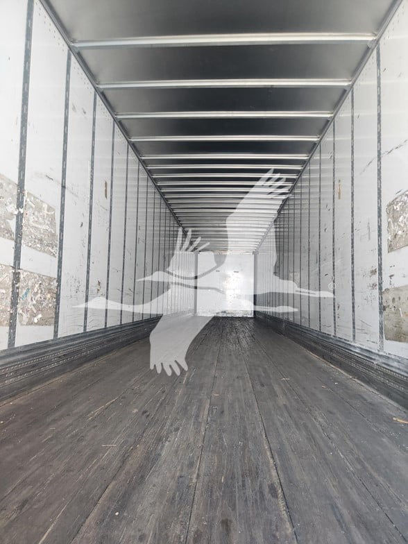 Inside trailer cargo area with wooden floor and metal walls, long empty space.