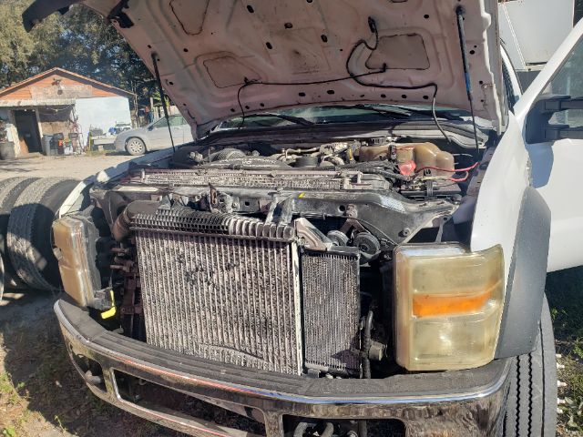 Front view of a 2008 Ford F550 with hood open, showing radiator, cooling fans, and engine bay components; left and right headlights visible; front bumper chrome; vehicle in mechanic yard.
