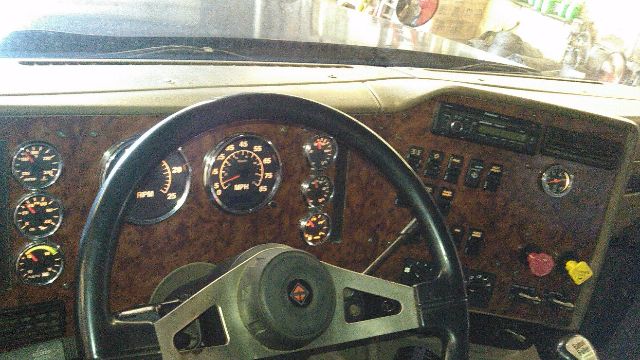 Truck interior dashboard with wood grain panel, steering wheel, gauges, and controls. Visible text includes various dials and a radio area, no clearly legible model-specific markings.