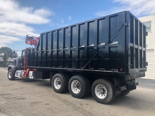 2014 Peterbilt 388 dump truck with a large black dump body, three rear axles, and a red cab area visible at the front left.