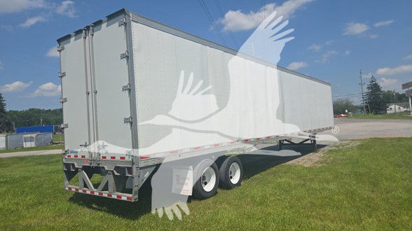 Trailer showing a large gray Vanguard post trailer with dual rear axles and R-17 style doors, parked on grass under blue sky.