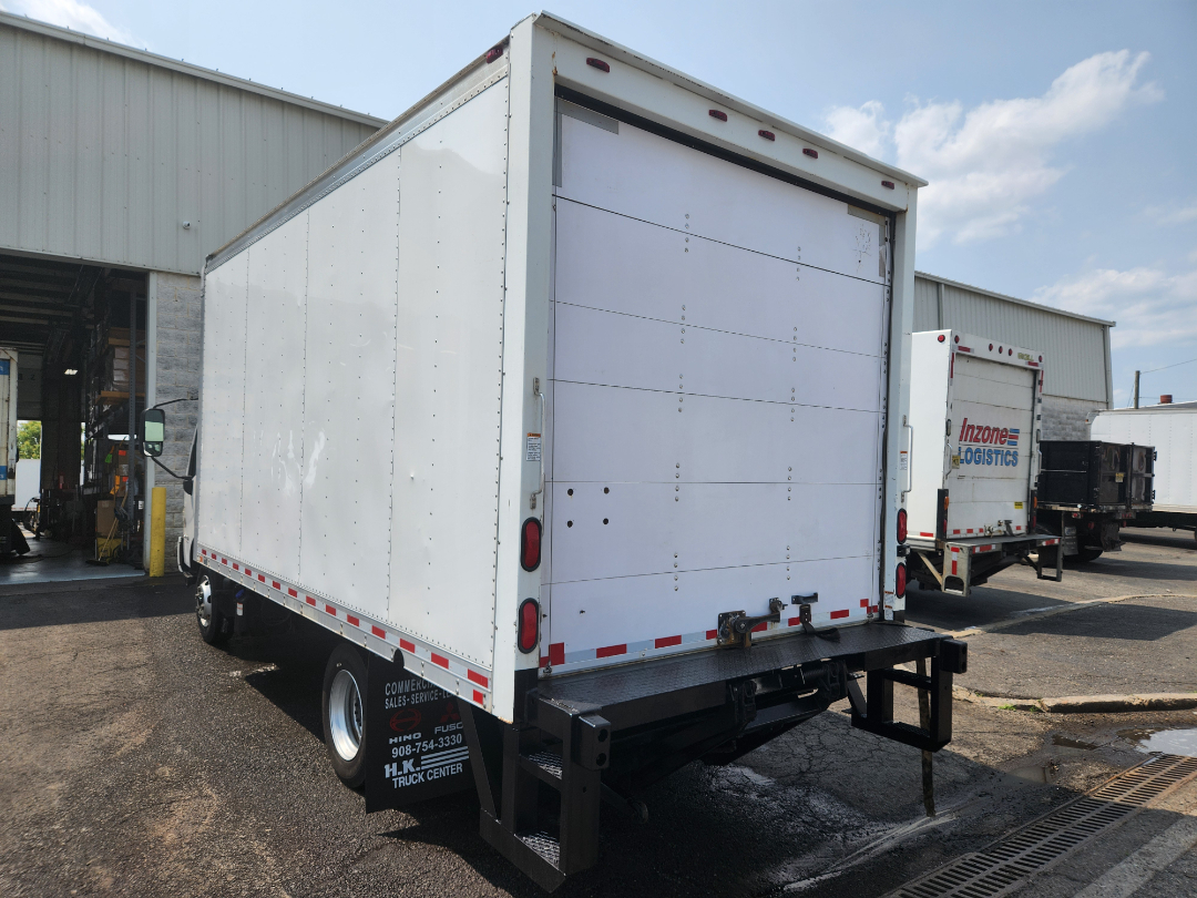 Box truck rear and side view showing white cargo box and rear doors, with a black bumper and lower step. Hino 155 image at a truck center.