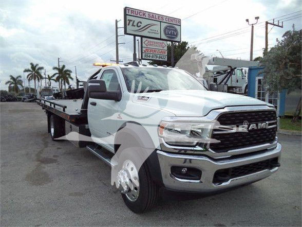 Ram 5500 tow truck with flatbed, front grille and bumper visible, dealership lot in background.
