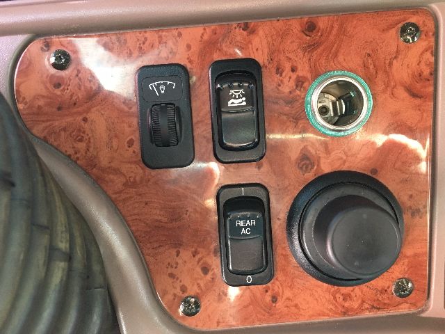 Peterbilt truck interior panel showing controls: left dial, center switches, rear A/C button, and a large round knob on woodgrain dash.