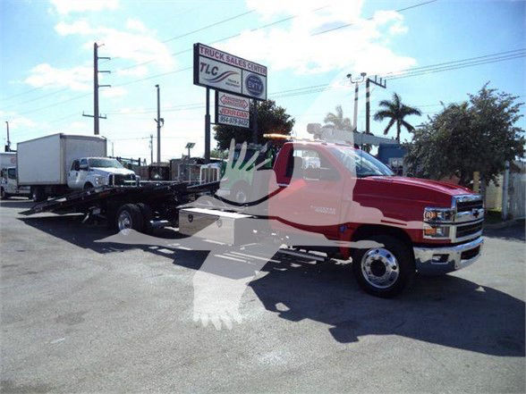 Red 2023 Chevrolet Silverado 6500HD tow truck in a lot with a flatbed trailer.