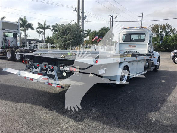 Peterbilt 337 flatbed tow truck in a dealership lot, rear view showing bed and hydraulic controls.