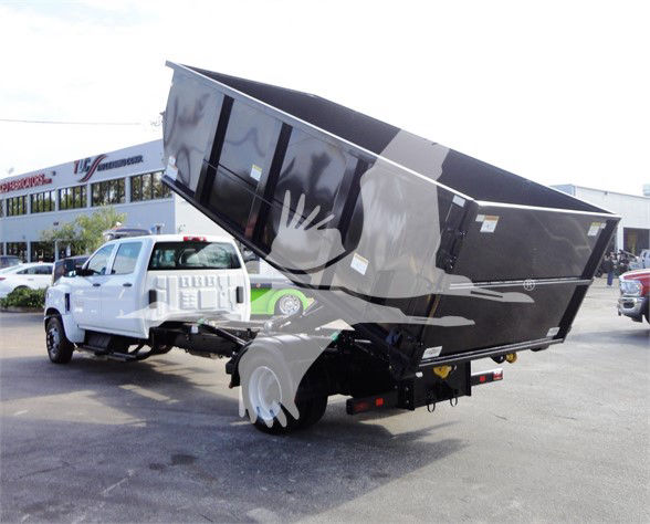 2023 Chevrolet Silverado 5500HD dump truck showing front cab and tilted dumping bed mounted on a white chassis with black container.