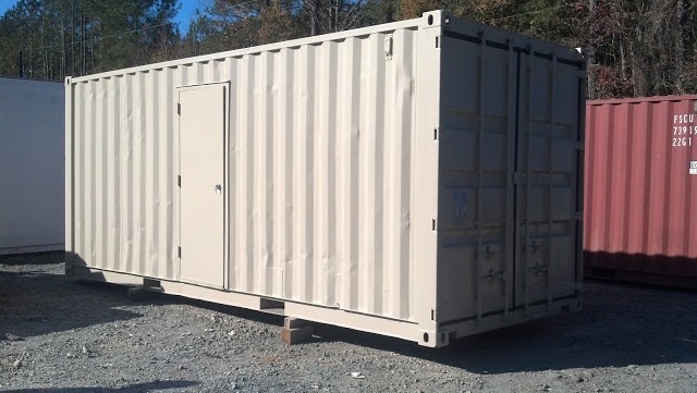 A beige shipping container used as a storage trailer with a side door and rear double doors, sitting on blocks in a gravel lot.