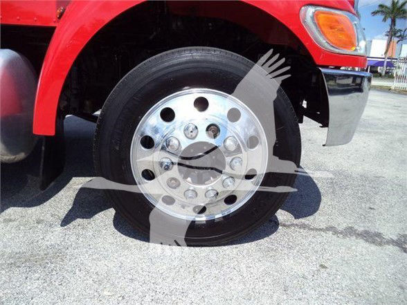 Front wheel of a red Peterbilt truck showing chrome alloy wheel and tire, with partial fender and bumper visible.