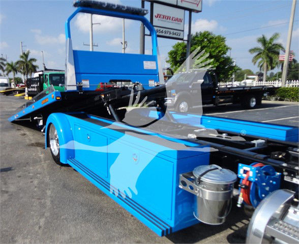 Tow truck flatbed chassis of a blue Peterbilt 337 with hydraulic winch and storage compartments, side view showing cab and long wheelbase.