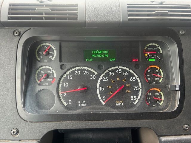 Dashboard cluster of a Freightliner Cascadia showing analog gauges, green digital odometer/readout in center, RPM, speed, and temperature gauges.