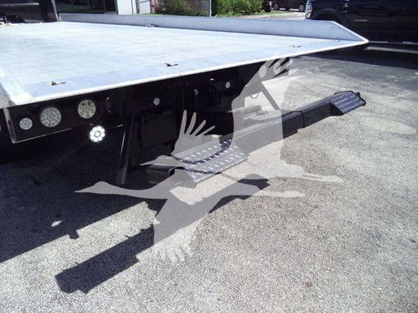 Isuzu NPR XD truck bed rear view with a flatbed platform and aluminum surface, tow hitch and side steps visible.