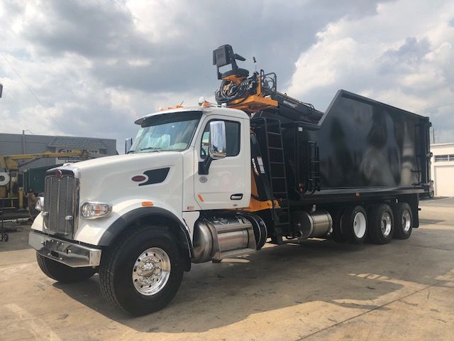 2019 Peterbilt 567 grapple truck with white cab and black dump body, orange crane on top.