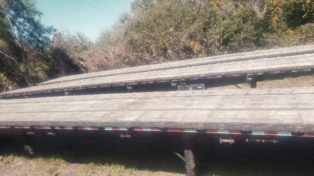 Flatbed trailer deck with stacked lumber, side rails, and support legs visible.