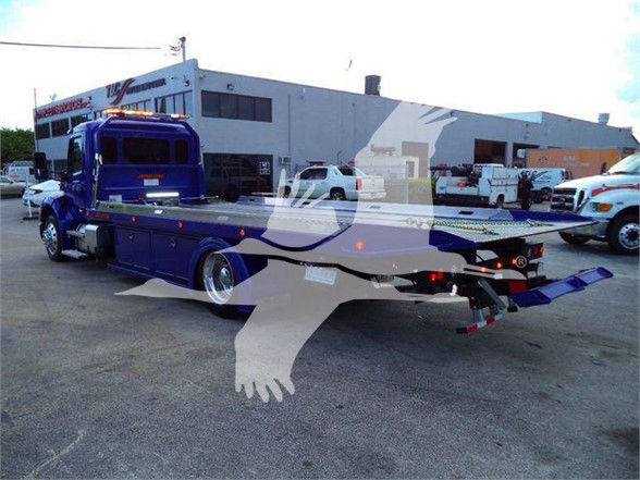 Tow truck bed with blue Peterbilt 536 in a dealership lot, stock BLUE536STEPSIDE visible