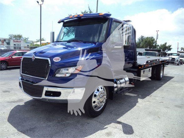 Tow truck: blue International MV cab with flatbed, chrome bumper, chrome wheel covers. Visible text on grille area and side panels but not legible in detail.