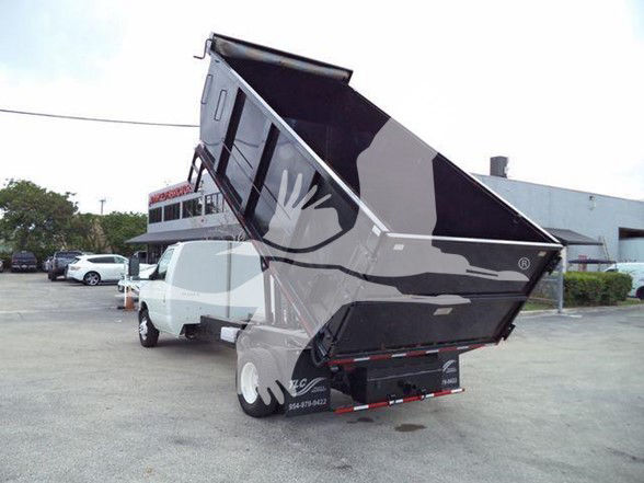 Ford E-450 dump truck with raised black dumping bed in a dealership lot.
