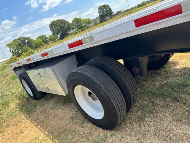Flatbed trailer rear dual wheels and aluminum toolbox mounted on side with reflective tape along edge.
