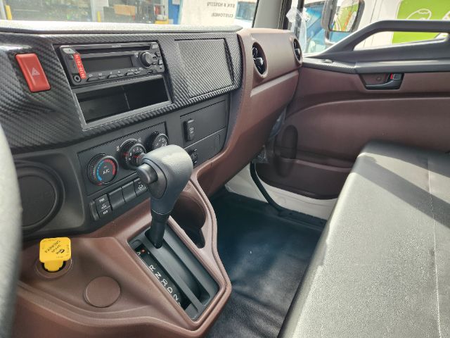 Interior of a 2025 Hino L6 cab and chassis showing gear shifter, climate controls, dashboard, and brown interior trim.