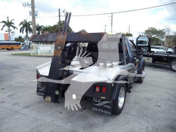 Tow truck bed with hydraulic hooklift arm and rear lights; Ford F-450 style chassis visible; watermark overlay obstructs some details.