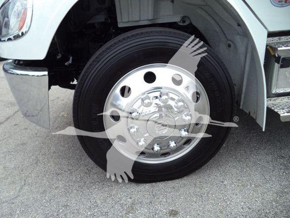 Front wheel and fender of a Freightliner M2 106 truck showing a chrome hubcap and black tire; partial view of wheel well and step. No visible text on components.