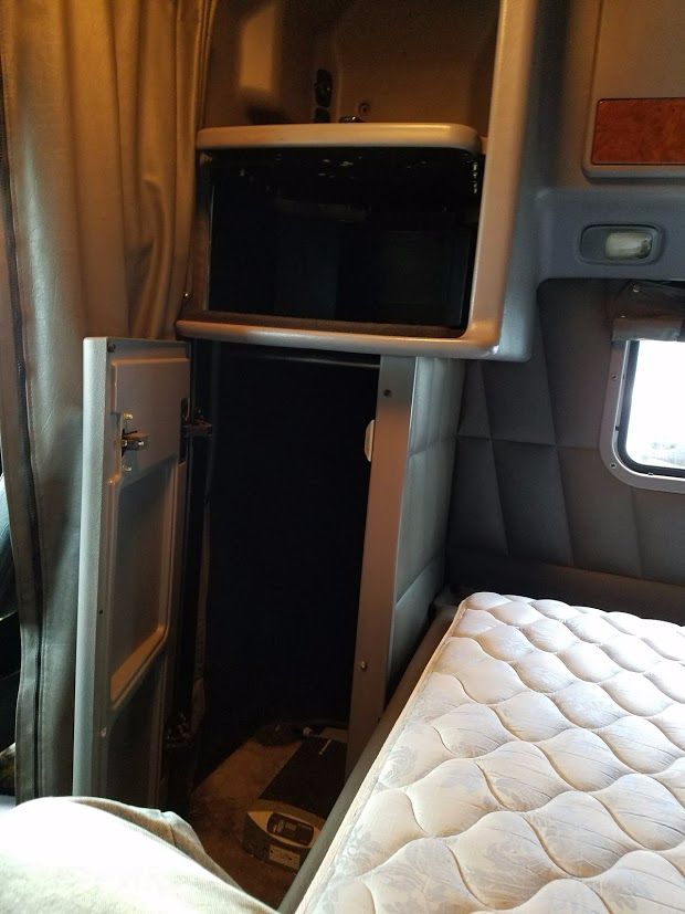 Peterbilt sleeper cab interior showing storage cabinet and doorway with bed in foreground.