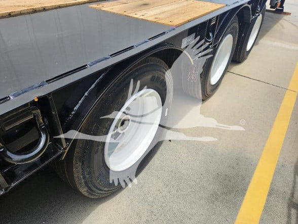 Flatbed trailer wheel assembly showing dual tires and white steel rims next to wooden deck edge.