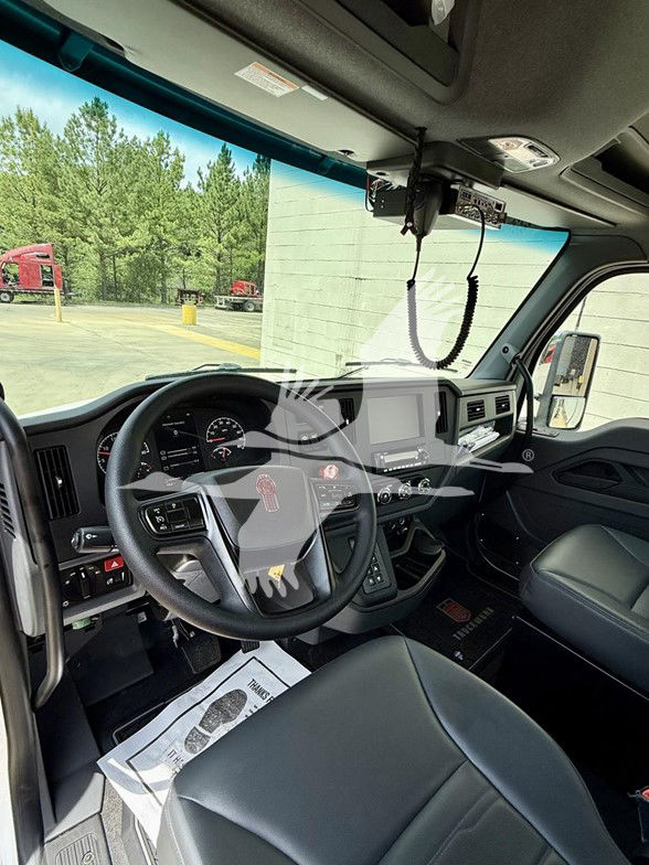 Kenworth T480 cab interior showing steering wheel with instrument cluster, center touchscreen, dashboard controls, visor, and hanging microphone cable.