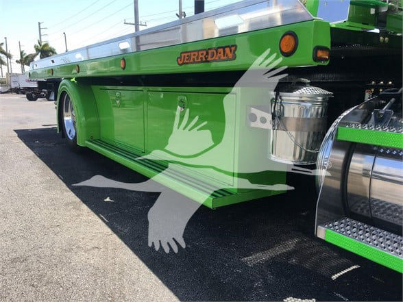 Side view of a bright green Peterbilt tow truck body with storage compartments, chrome fuel tanks, and JERR-DAN branding on the side.