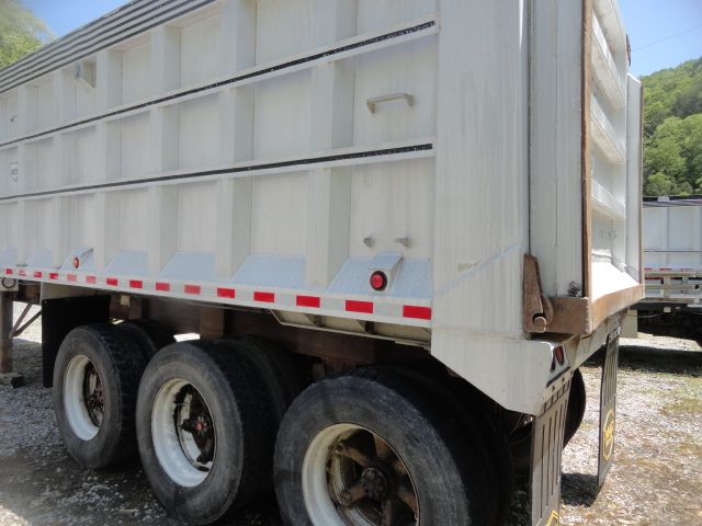 Dump trailer with triple-axle wheels and white metal sides, red/white reflective strip along the lower edge, rear gate, and rugged tires.